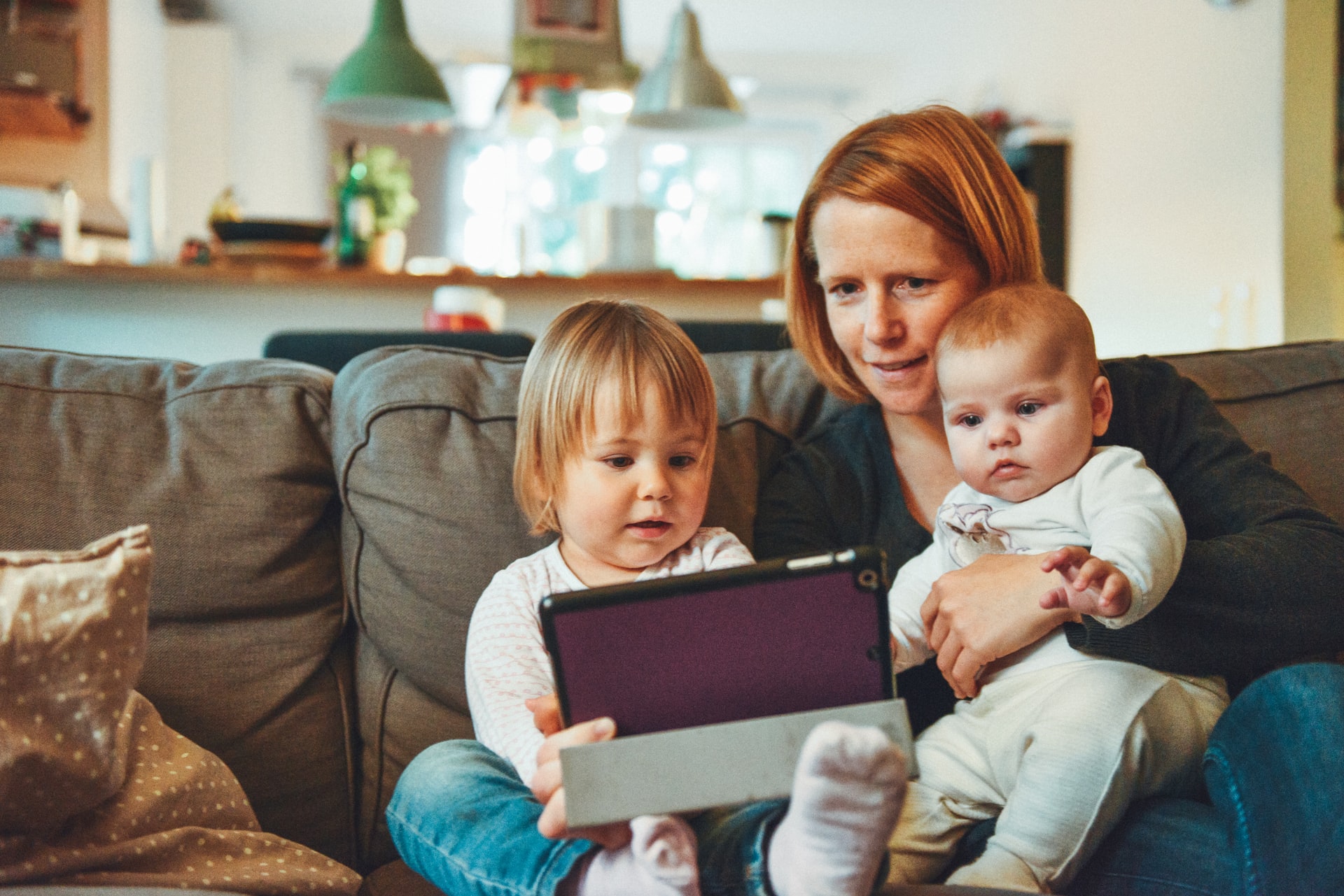 Mom on tablet with baby and toddler on lap